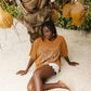 Woman sitting on a sandy beach with brown oversized t-shirt with baby blue graphic 