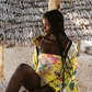 Woman in a colorful yellow one-piece swimsuit sitting under a thatched roof