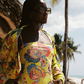 Woman in a colorful yellow swimsuit standing under a thatched roof with palm trees in the background