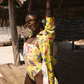 Woman in a yellow swimsuit with a colorful scarf standing under a thatched roof.