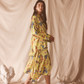 Woman in a yellow floral set standing against a beige curtain backdrop