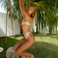 Woman in a colorful yellow bikini standing on a rock with palm trees in the background