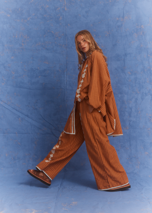 Person wearing a orange and brown striped shirt and pant set against a blue background