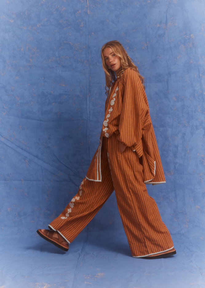 Person wearing a orange and brown striped shirt and pant set against a blue background