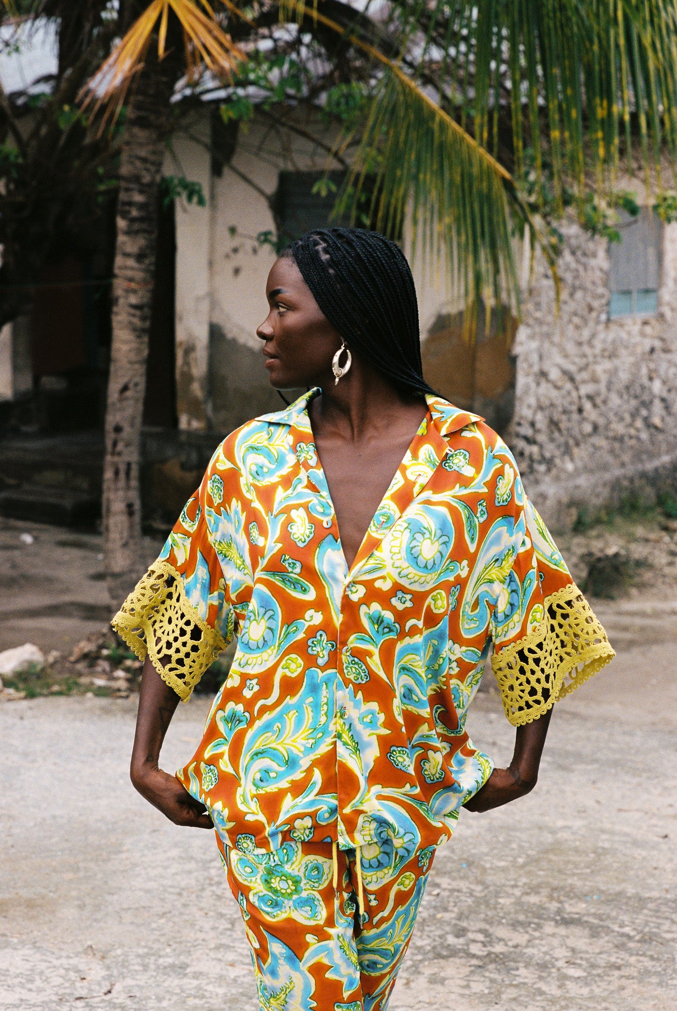 Woman wearing vibrant citrus orange, aqua and lime floral resort shirt with lime green crochet lace cuffs, slinky fabric, and relaxed oversized fit.