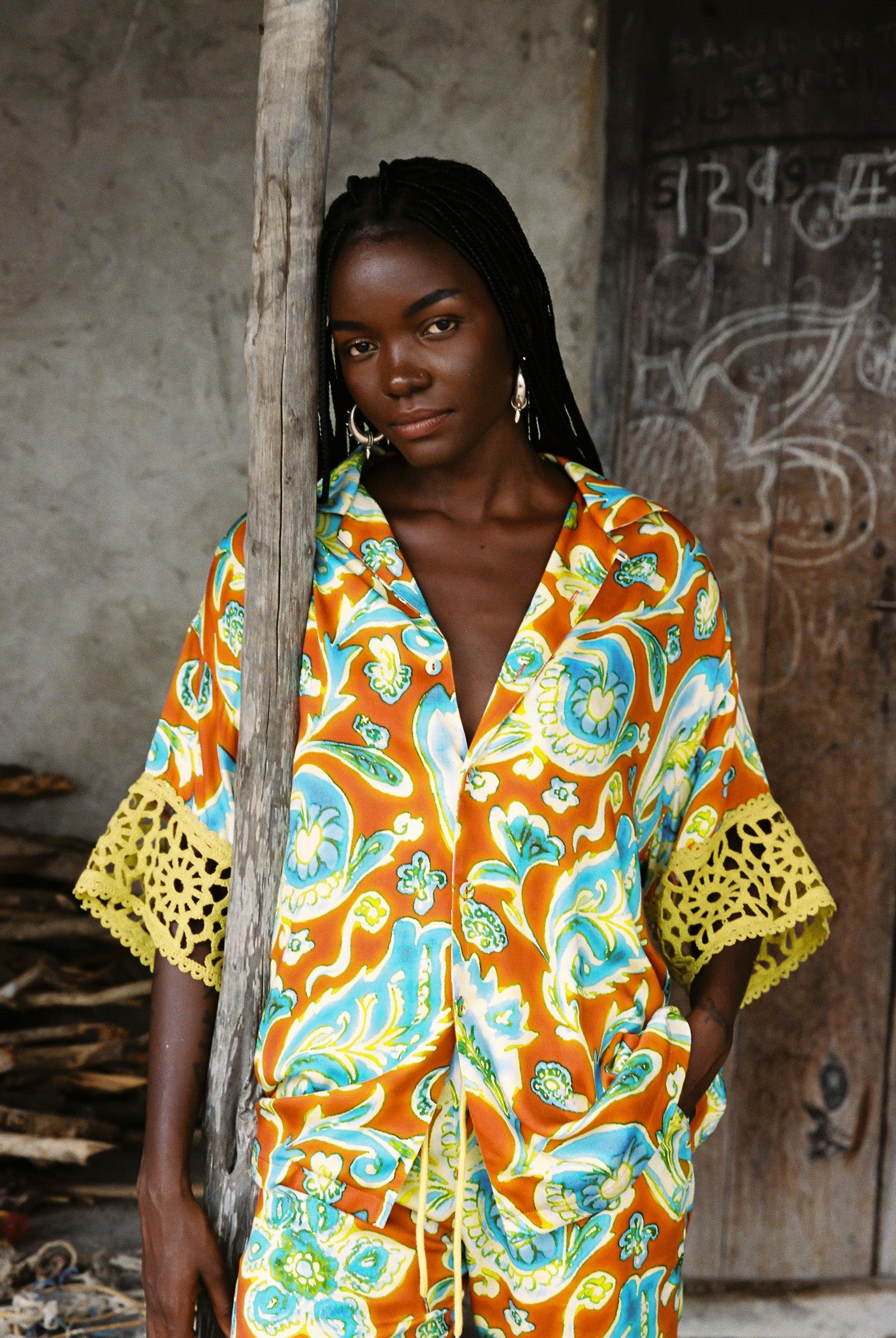 Woman wearing vibrant citrus orange, aqua and lime floral resort shirt with lime green crochet lace cuffs, slinky fabric, and relaxed oversized fit.