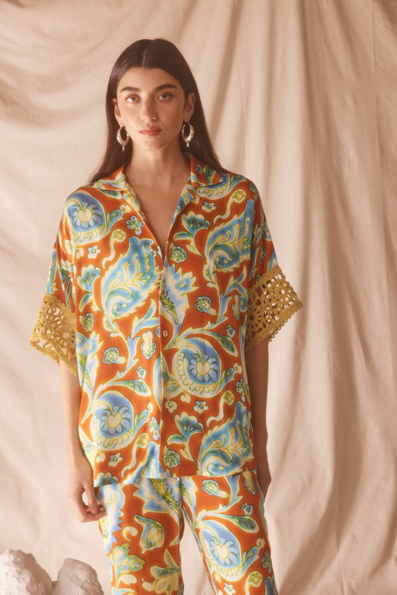 Woman wearing vibrant citrus orange, aqua and lime floral resort shirt with lime green crochet lace cuffs, slinky fabric, and relaxed oversized fit.