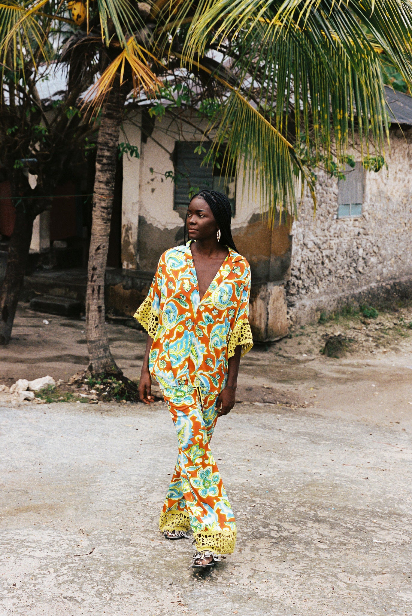 Woman wearing colourful orange, blue and green print flared pant and shirt set with green lace trim detailing