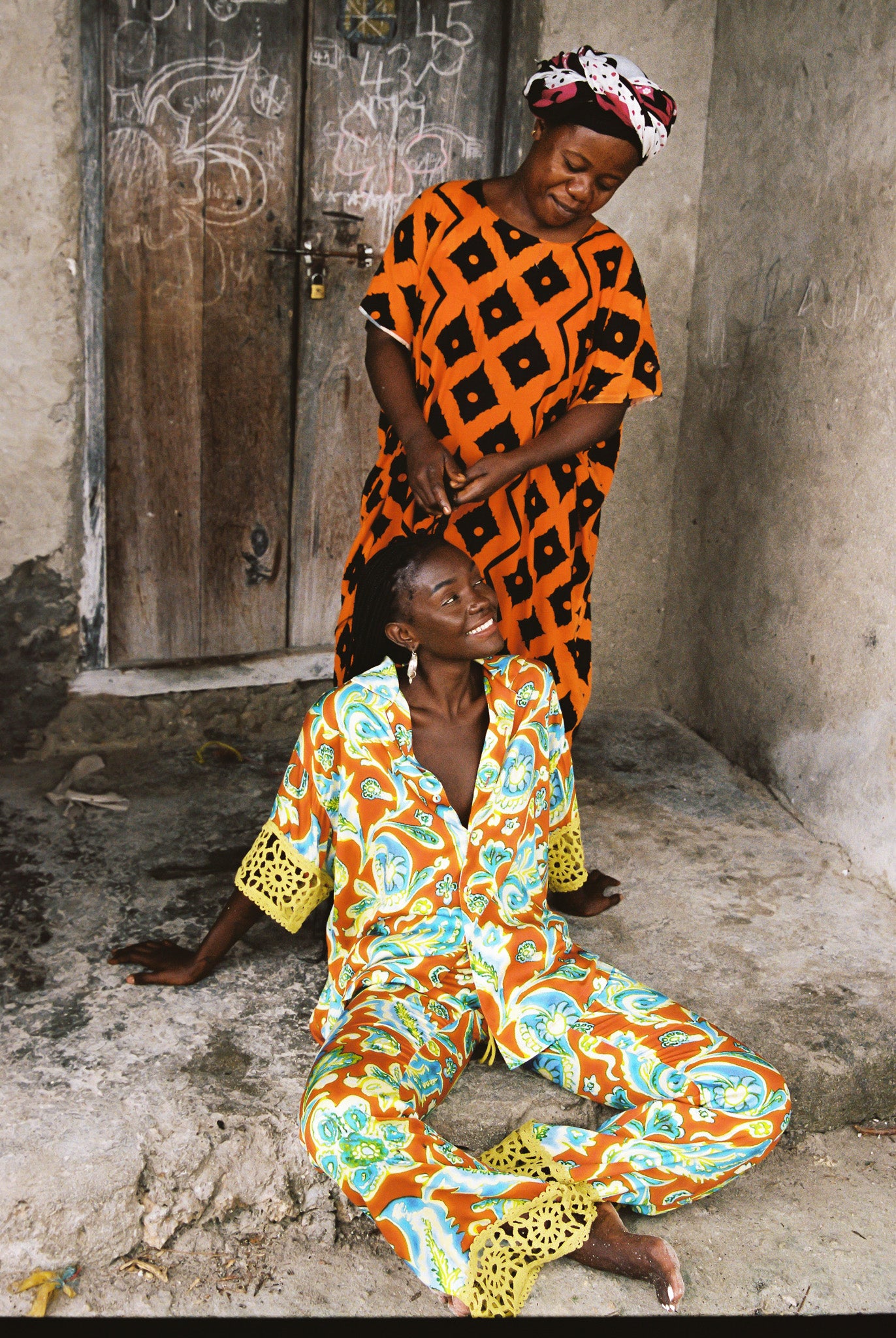 Woman wearing colourful orange, blue and green print flared pant and shirt set with green lace trim detailing