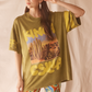 Person wearing a lime green desert graphic t-shirt with colorful pants against a plain background