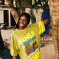 Woman wearing a bright lime green t-shirt with desert text and graphics, standing outdoors near trees.