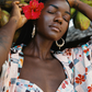 Woman with a red flower in her hair, wearing a colorful pink bikini and patterned cover-up, surrounded by coconuts.
