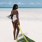 Woman in a pink patterned swimsuit holding a palm leaf on a tropical beach