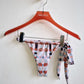 Multicolored patterned bikini bottom on a red hanger against a white background