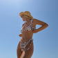 Woman in a pink checkered bikini and sun hat against a clear blue sky