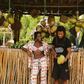 Two people standing in front of a rustic wooden structure with coconuts and tropical plants. Women is wearing pink patterned set and bikini top. 