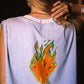 A person shown from the back wearing a sleeveless periwinkle top with a large orange and green flame graphic printed on the back. The brand name 'KINGA CSILLA' is printed in white along the inside neckline.