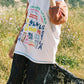 Person wearing a white t-shirt with colorful text and graphics, standing in a natural setting.