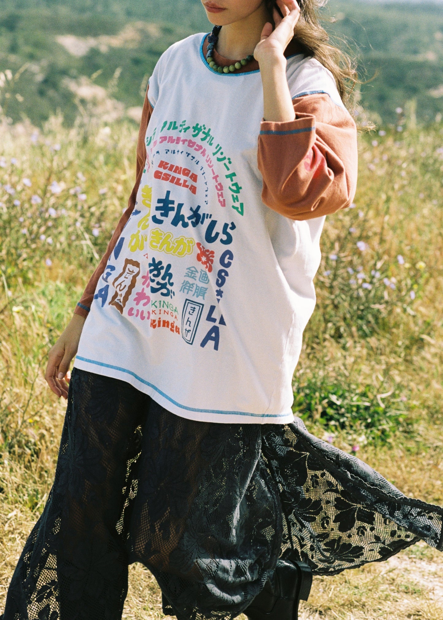 Person wearing a white t-shirt with colorful text and graphics, standing in a natural setting.