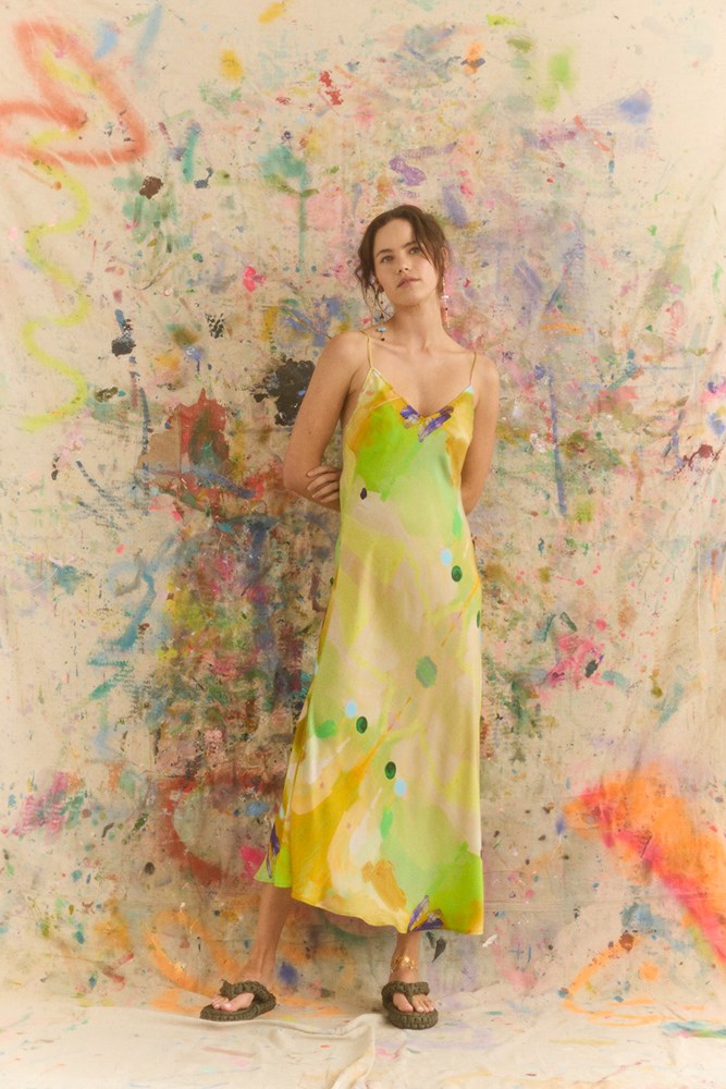 Woman in a colorful dress standing against a abstract, multicolored wall.