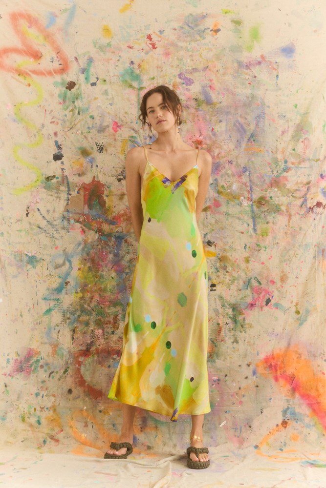 Woman in a yellow dress standing against a colorful abstract wall.