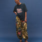Person wearing a black t-shirt with colorful text and patterned harem pants on a blue background