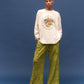 Person wearing a white sweatshirt with colorful design and green pants on a blue background