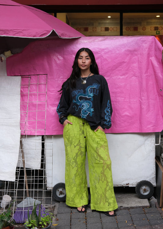 Person wearing a black sweatshirt with blue design and bright green pants standing under a pink canopy.