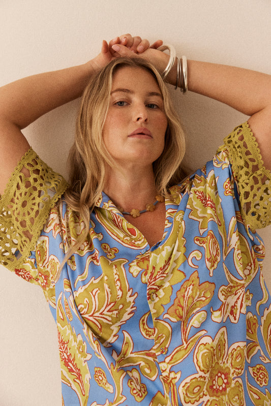 Woman wearing a colorful patterned top with her arms raised against a neutral background