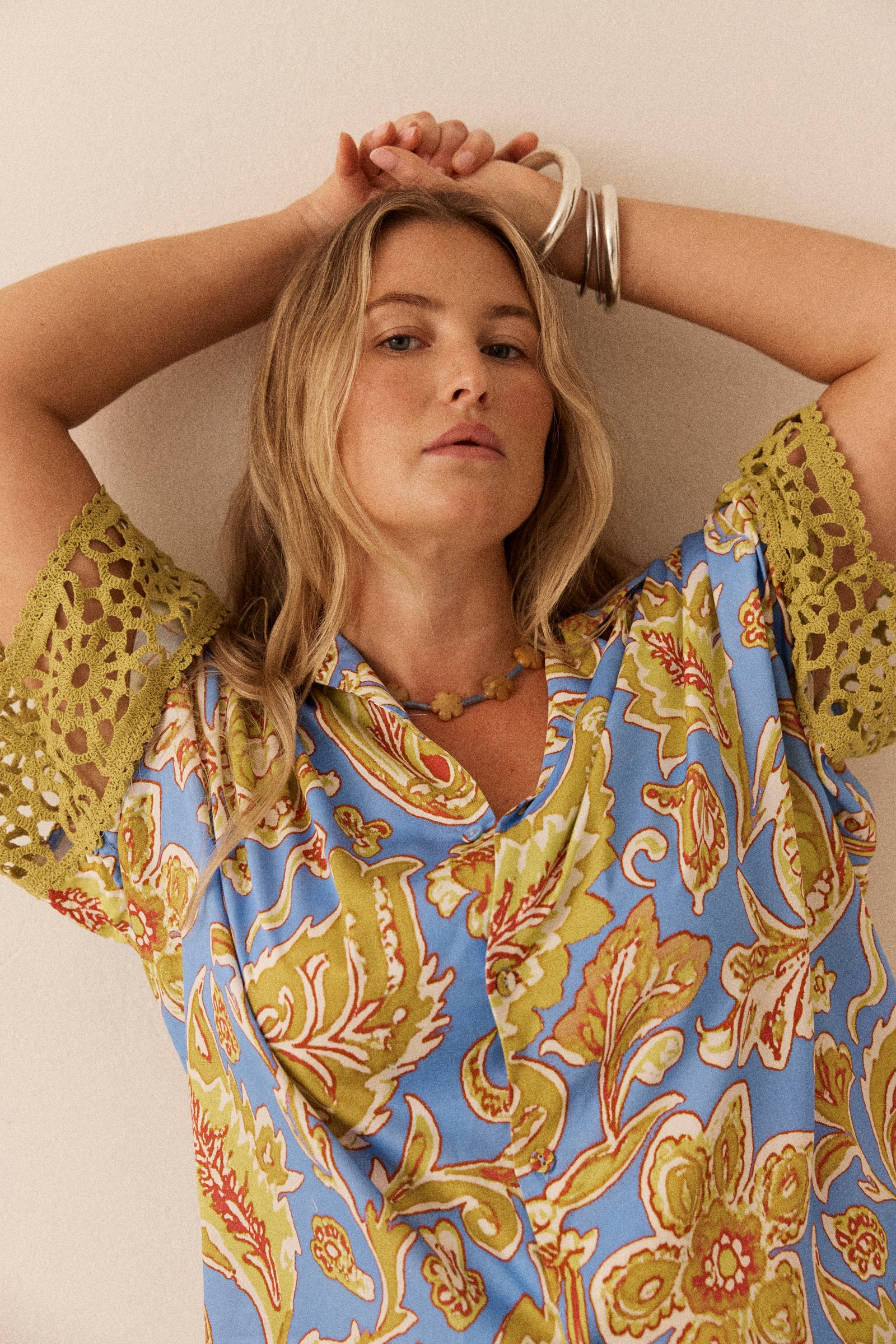 Woman wearing a colorful patterned top with her arms raised against a neutral background