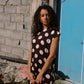 Woman in a polka dot dress standing against a textured wall with a blue door.