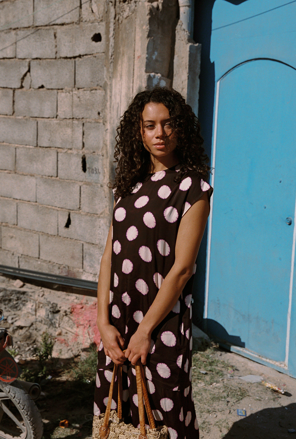 Woman in a polka dot dress standing against a textured wall with a blue door.