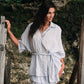 Woman in a light blue romper standing outdoors with greenery in the background