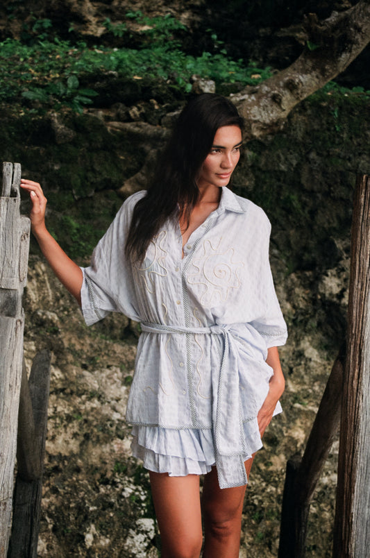 Woman in a light blue romper standing outdoors with greenery in the background