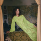 Woman in a green dress standing in a room with patterned walls and curtains.