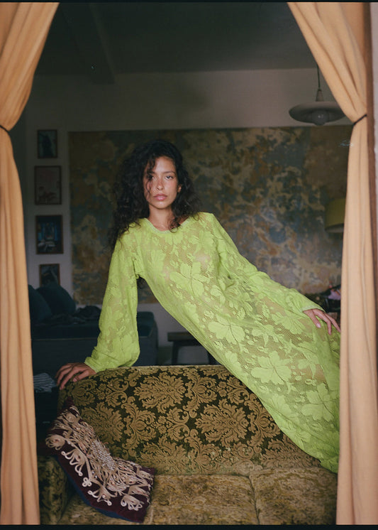 Woman in a green dress standing in a room with patterned walls and curtains.