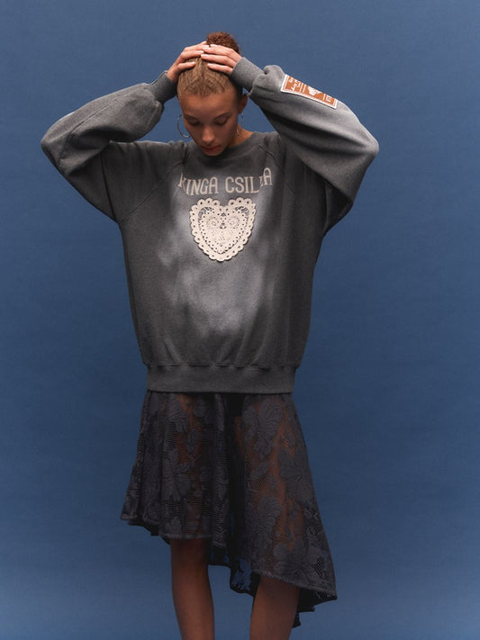 Person wearing a gray sweatshirt with a heart design and text, standing against a blue background