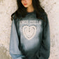Woman wearing a gray sweatshirt with 'KINGA CSILLA' and a heart design against a textured wall.