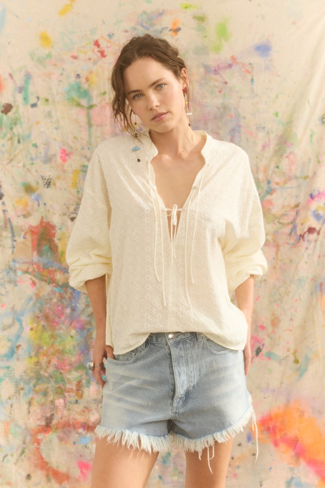 Woman wearing a white blouse and denim shorts against a colorful abstract background