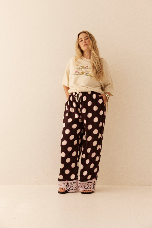 Woman wearing a beige sweatshirt and black polka dot pants with lace trim on a white background