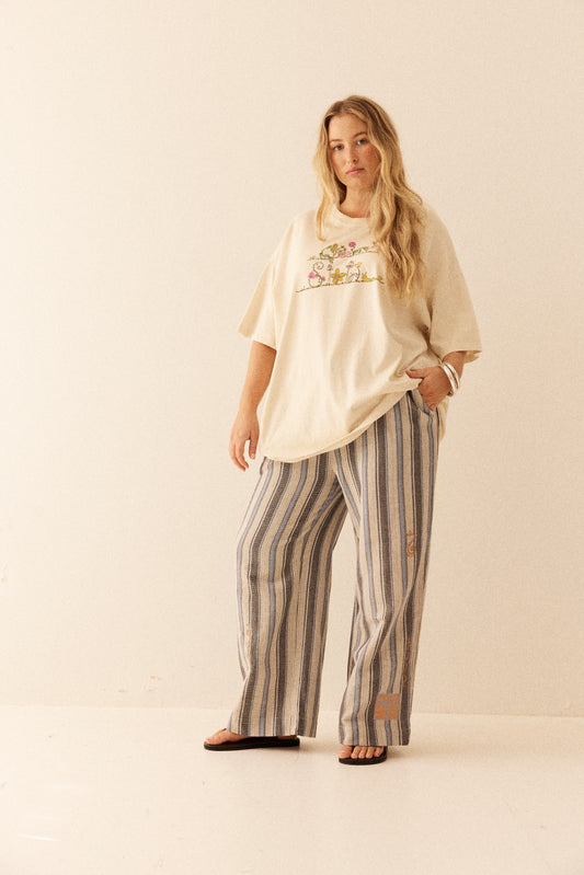 Woman wearing a beige top with floral design and striped pants on a white background