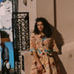 Woman in a patterned dress standing against a building with a decorative metal gate.