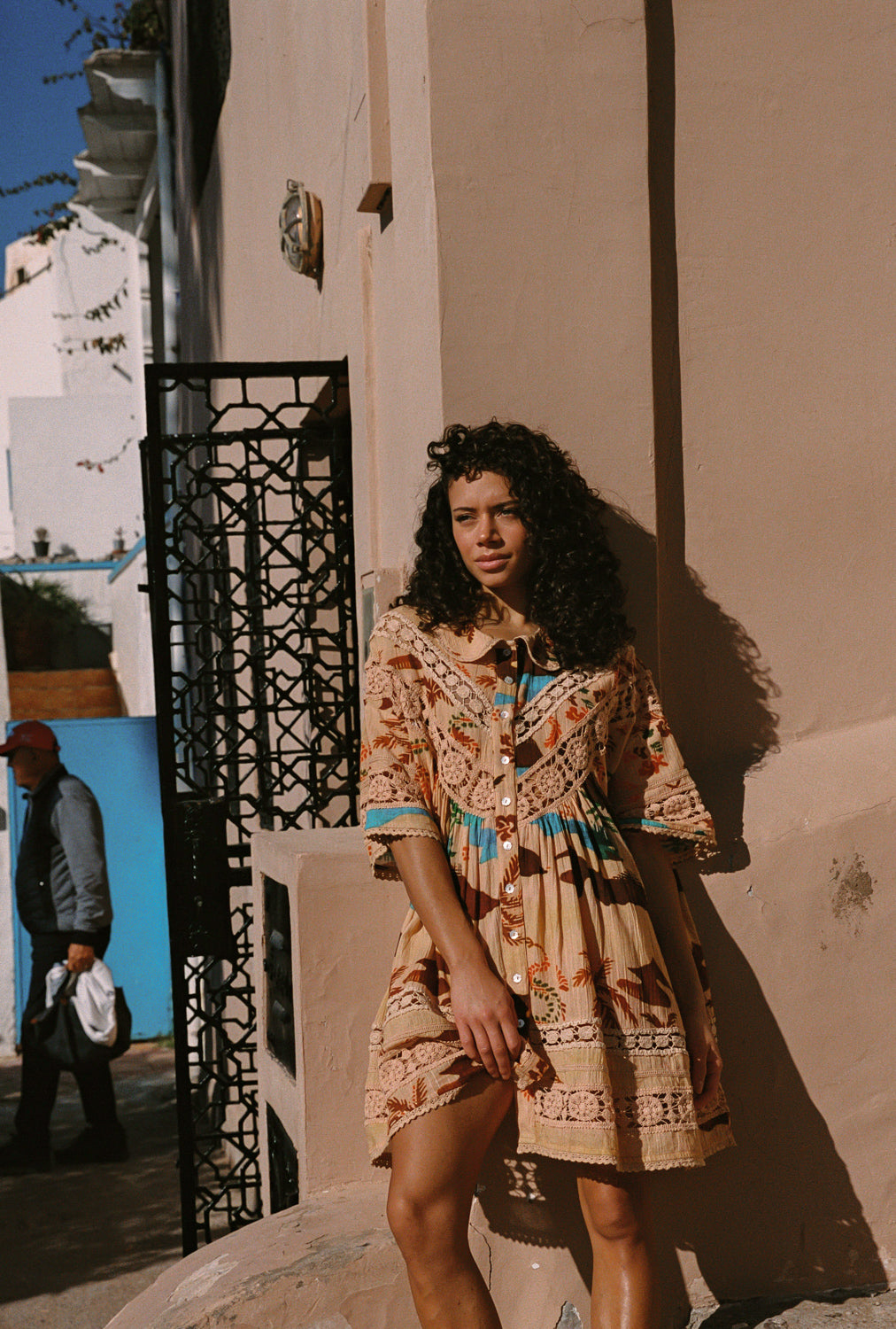 Woman in a patterned dress standing against a building with a decorative metal gate.