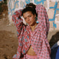 Woman in a pink floral outfit sitting against a textured wall with graffiti.