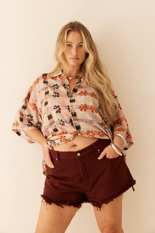 Woman wearing a patterned shirt and maroon shorts against a plain background