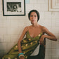 Woman in a green polka dot dress sitting on a chair against a tiled wall with framed pictures.