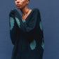 Person wearing a dark green cardigan with teal patterns against a blue background