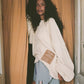 Woman wearing a white sweatshirt with a patch and blue shorts standing in front of a curtain.