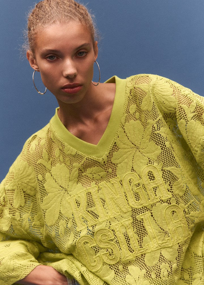 Woman wearing a bright yellow lace sweater against a blue background