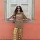 Woman wearing a green t-shirt and patterned pants standing against a pink wall with white shutters.